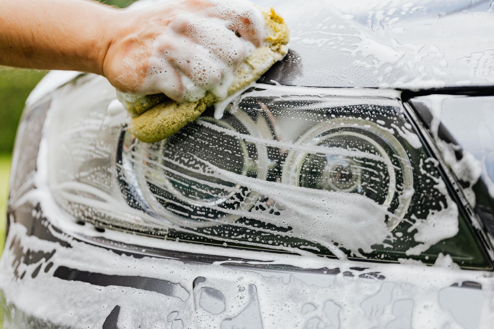 Hand detailing a car headlight with soap and sponge